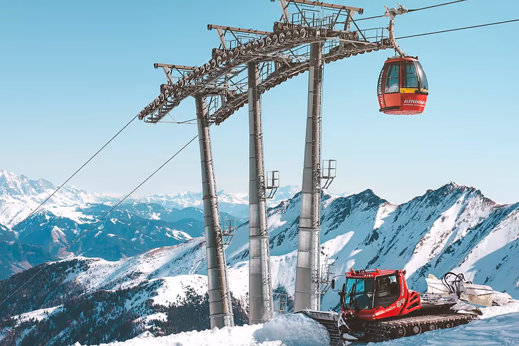 Rød gondol og snøscooter blant snødekte fjell