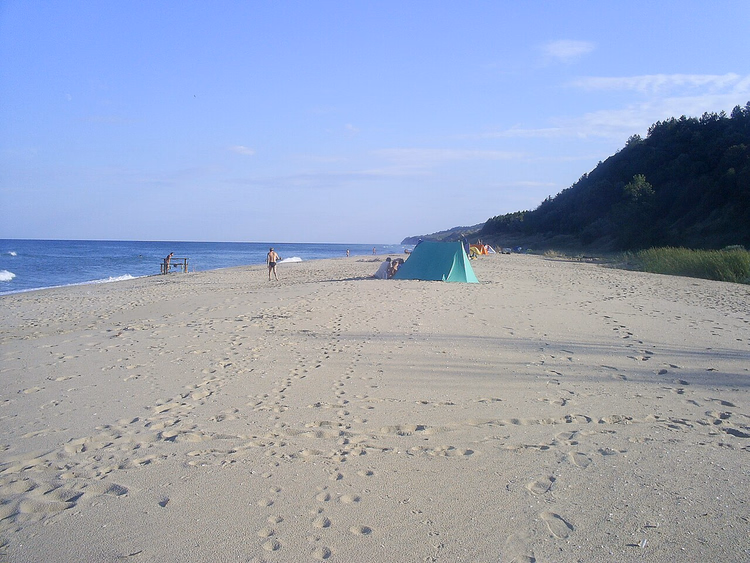 Wild zandstrand met een tent bij een beboste helling