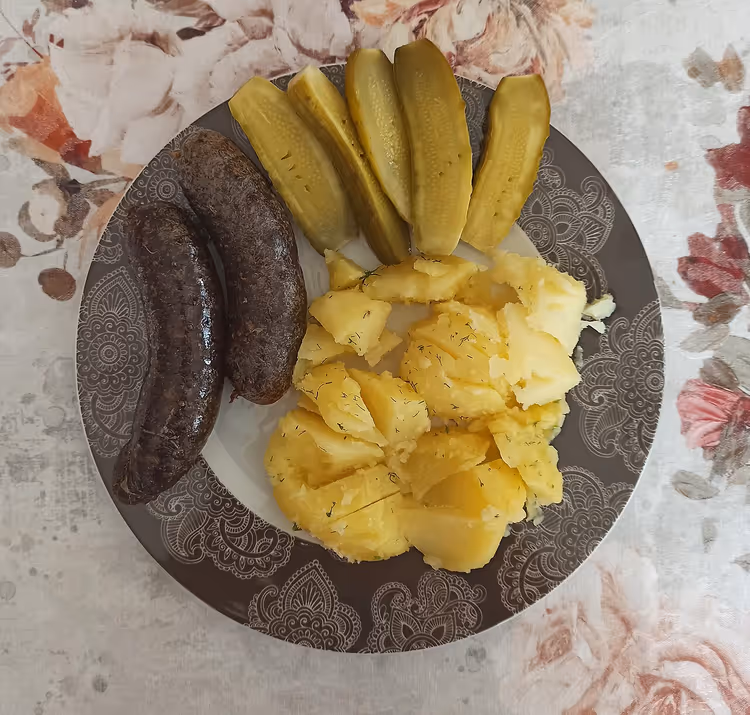 Kaszanka met aardappelen en augurken op een bord