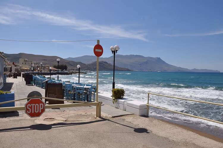 Strandpromenade med taverna, STOPP-skilt og havutsikt