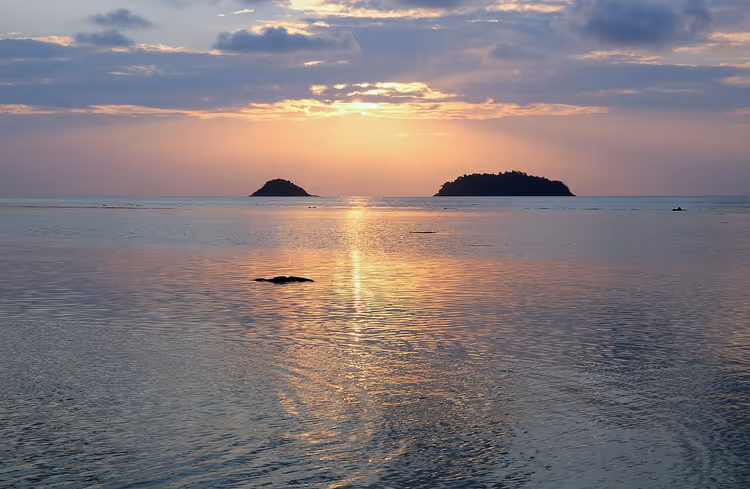 Solnedgang over havet og to småøyer ved horisonten