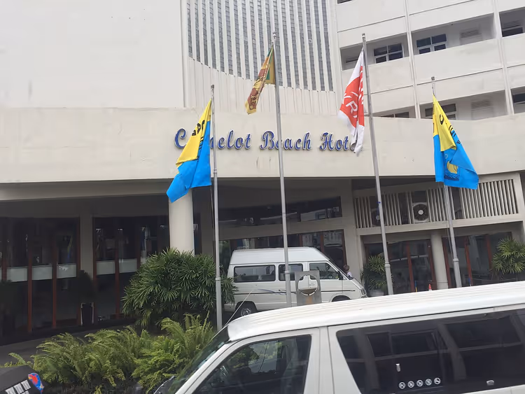 Exterieur van Camelot Beach Hotel met vlaggen en auto's