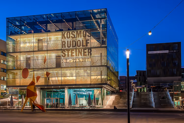 Стеклянное здание Kunstmuseum Stuttgart ночью с баннером выставки