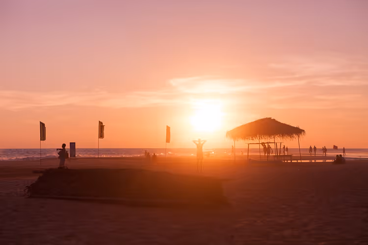 Strand bij zonsondergang met een luifel en silhouetten van mensen