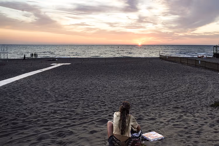 Marina di Donoratico plajında gün batımı, kumda bir kadın