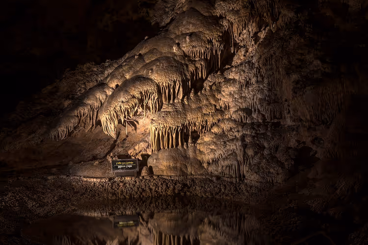 Grotte med stalaktitter og speiling i mørkt vann