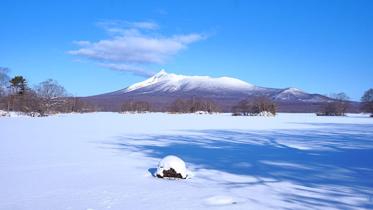 Verschneiter Berg Komagatake über einem zugefrorenen See