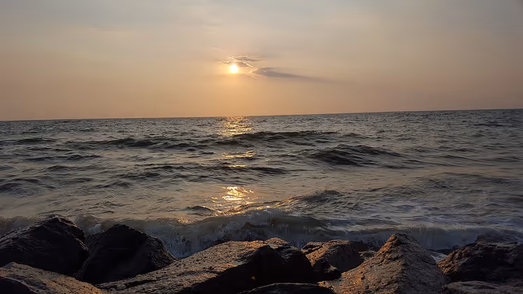Zonsondergang boven de oceaan en golven bij een rotsachtige kust