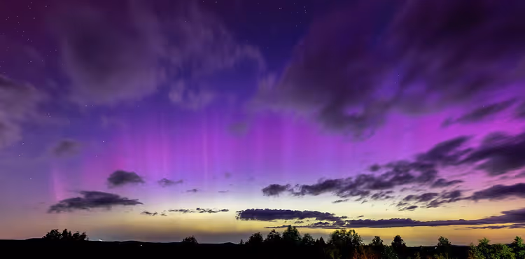 Paars noorderlicht boven een bos en wolken