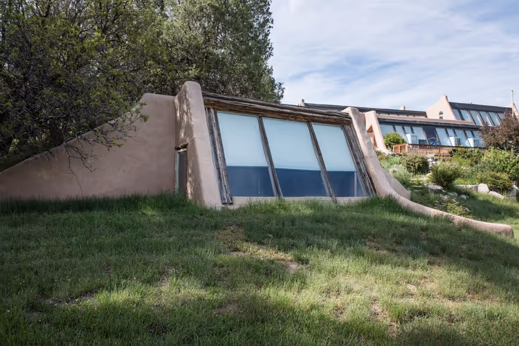 Çimenli bir tepede eğimli camlı Earthship evi