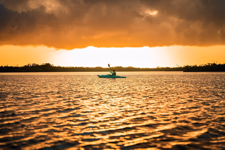 Persoon in kajak op het water bij zonsondergang