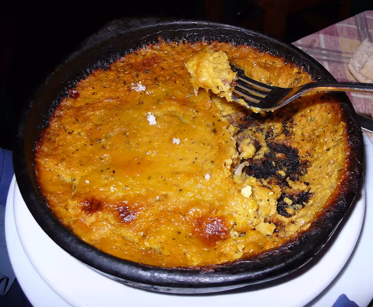 Gratinert pastel de choclo i en stekepanne med en gaffel