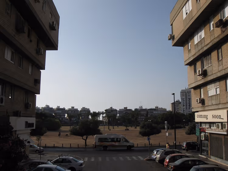 إطلالة على ساحة مع أشجار وموقف سيارات ومبانٍ