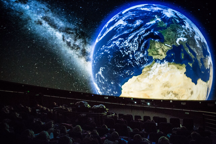 Projectie van de aarde op de planetariumkoepel, publiek in de zaal