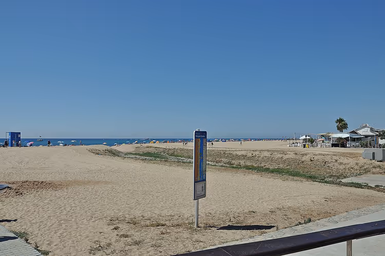 Strand med sand, hav og et skilt på stranden