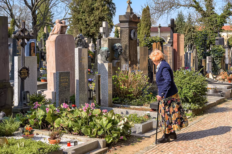 Oudere vrouw wandelt over een pad op de begraafplaats Vysehrad tussen de grafstenen