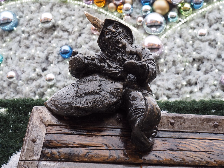 Bronzener Prezentuś-Zwerg vor einem Weihnachtsbaum