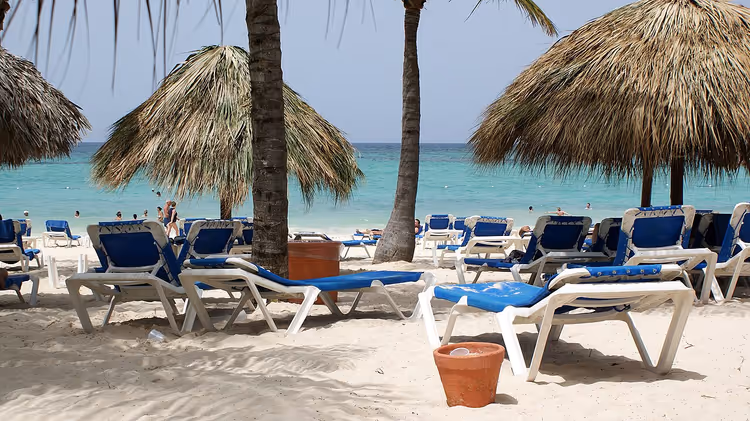 Strand med solsenger og parasoller av palmeblader