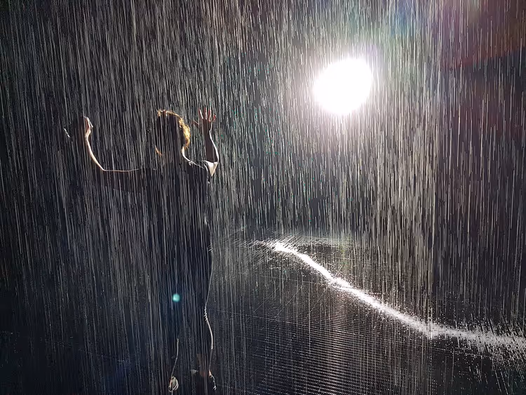 Dunkler Raum mit Wasserströmen in der Installation Rain Room