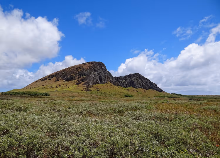Gresskledde skråninger på Rano Raraku-vulkanen under en skyet himmel