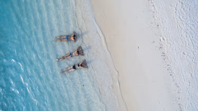 Drie mensen ontspannen in turquoise water vlak bij een strand