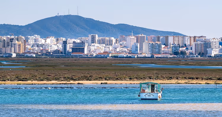 Lagune der Ria Formosa mit einem Boot und der Stadt Faro