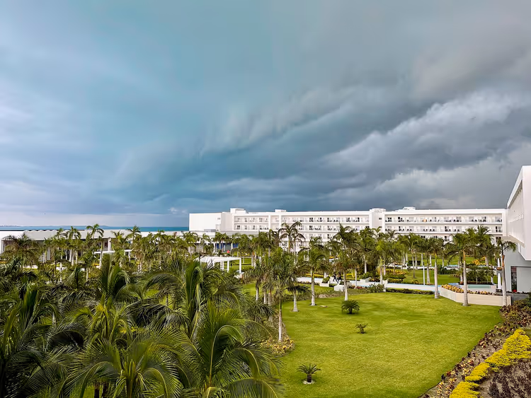 Hvit hotellbygning blant palmer under en stormfull himmel