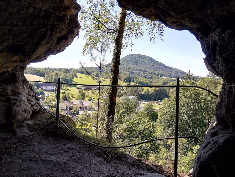 Blick aus einer Höhle auf Dorfhäuser und den Růžovský vrch