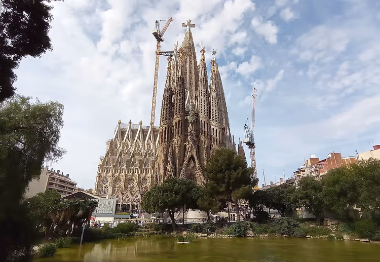 Sagrada Familia met bouwkranen en een vijver ervoor
