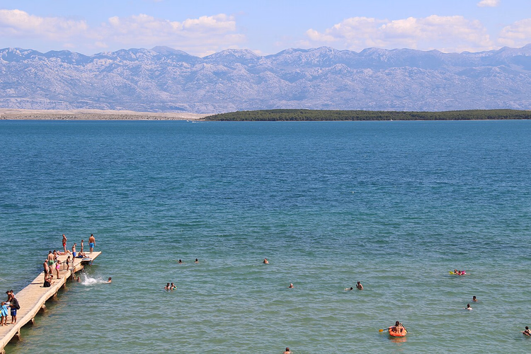 Badende nær en brygge med Velebit-fjellene i bakgrunnen