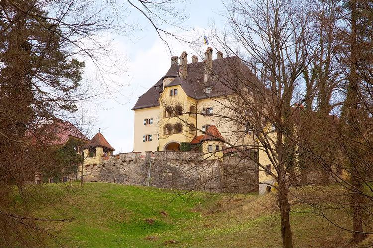 Gelbes Schloss Glanegg auf einem Hügel, umgeben von Bäumen
