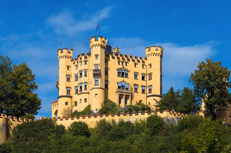 Geel kasteel Hohenschwangau op een beboste heuvel