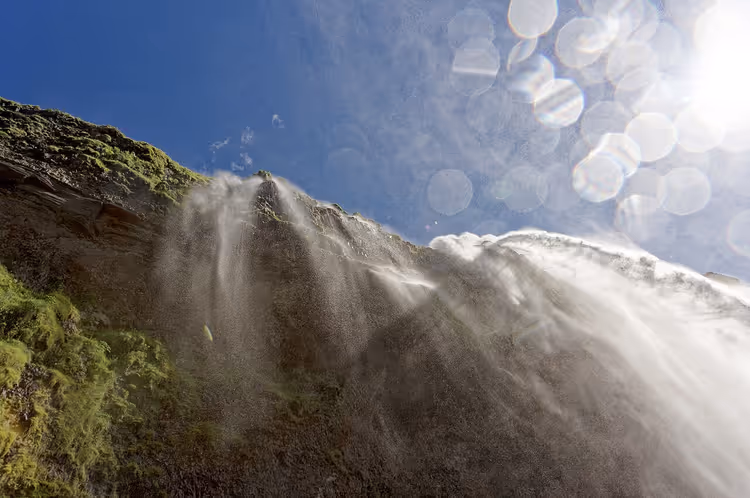 Seljalandsfoss-vesiputous, jossa vesisumua ja auringon heijastusta