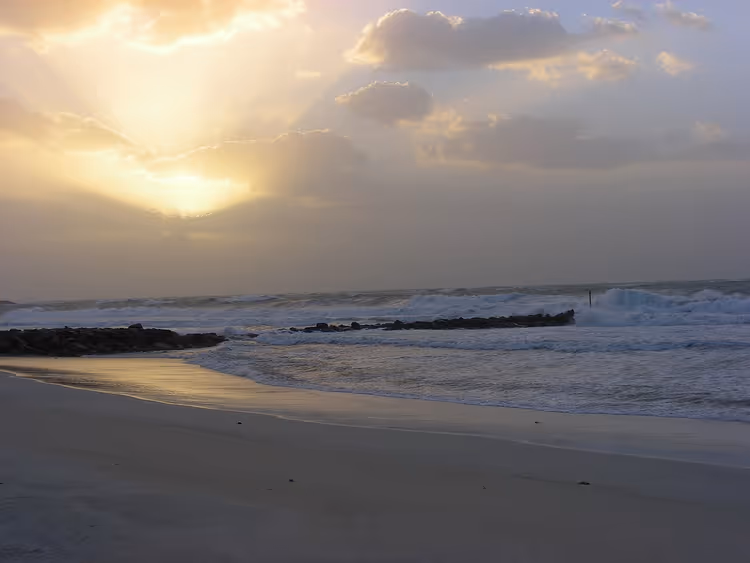 Solnedgang over Sharjah Beach med bølger og svaberg