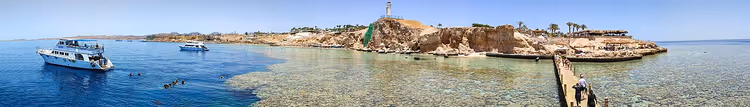 Panorama van een baai met boten, een pier en een vuurtoren op een rots