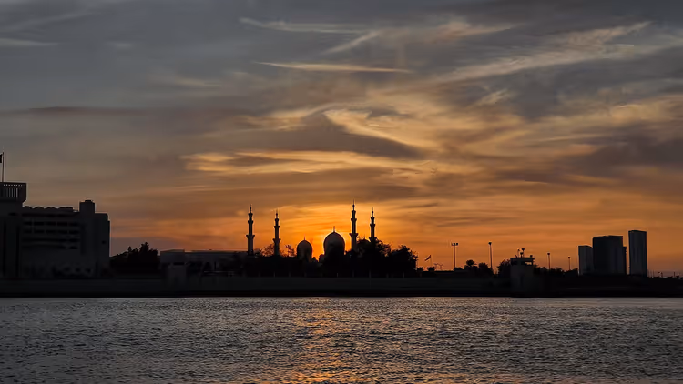 Gün batımında su üzerinde minareli bir caminin silueti