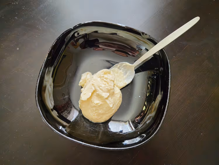 Siyah bir kasede beyaz kaşıkla servis edilen koyu kıvamlı skyr