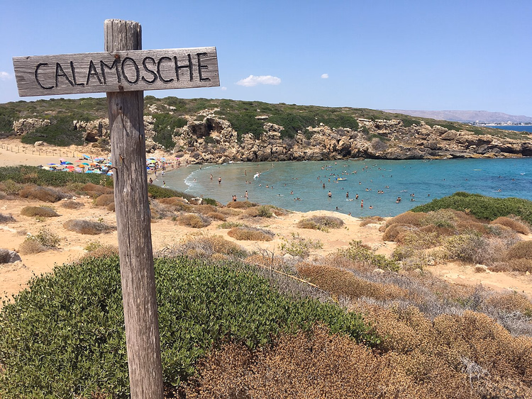 Yüzücülerle turkuaz bir koyun üzerinde Calamosche tabelası