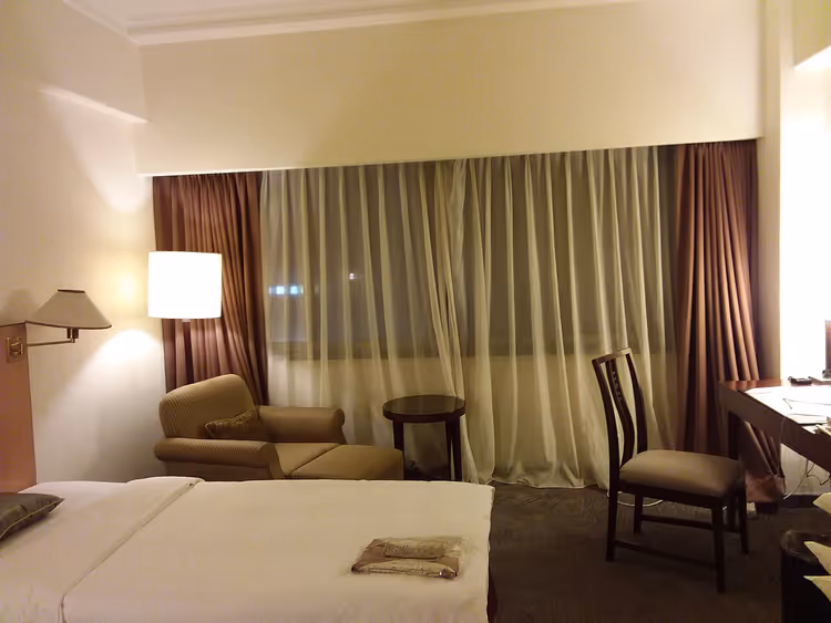 Hotelkamer met bed, fauteuil, gordijnen en tafel