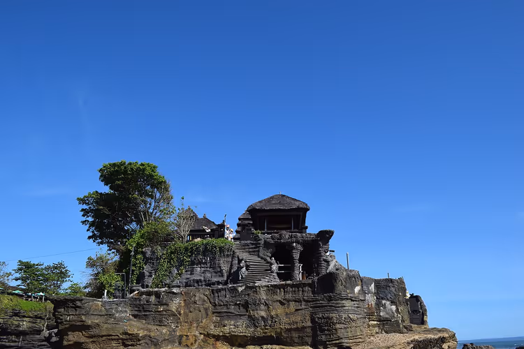 Pura Tanah Lot-tempelet på en klippe under en blå himmel