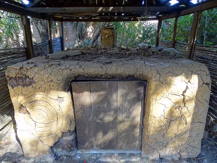 Temazcal-koepel van klei met een houten deur onder een palapa