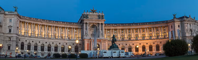 Geschwungene Fassade der Hofburg bei Nacht mit Reiterstandbild auf dem Platz