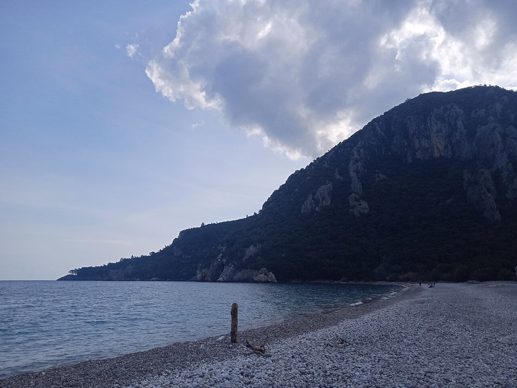 Praia de seixos sob uma montanha arborizada perto de Olympos