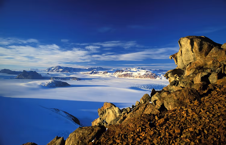 Klippefulle fjell og snødekt slette under en blå himmel