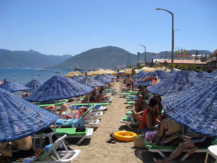 Dağların yakınında mavi şemsiyeler ve şezlonglarla plaj