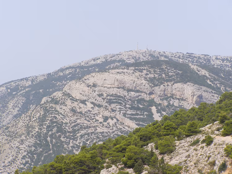 Çam ağaçlarıyla kaplı kayalık tepe ve antenlerle zirve