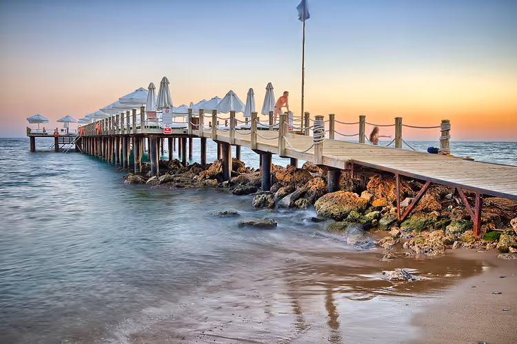 Holzsteg mit Sonnenschirmen bei Sonnenuntergang am Strand