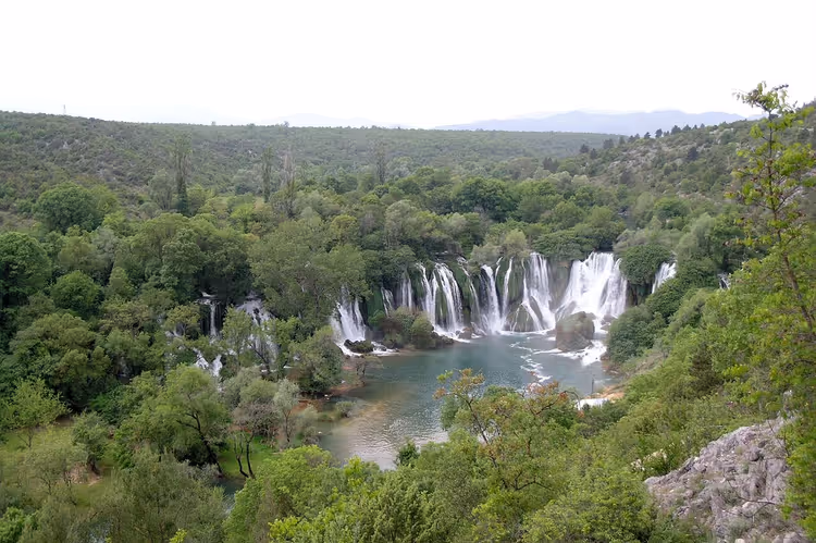 Kravica-Wasserfälle stürzen zwischen grünen Hängen und einem See herab
