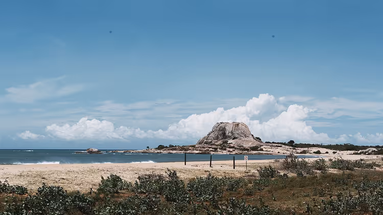 Playa de arena, océano y una roca en Yala