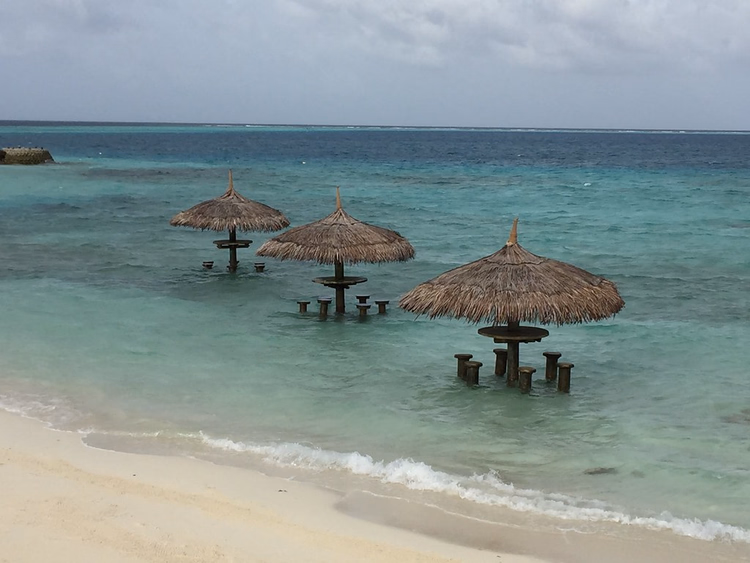 Rieten parasols met tafels midden in de turquoise lagune